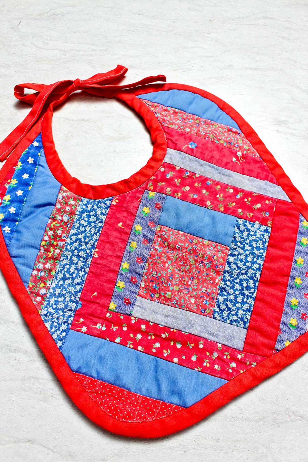 Completed baby bib with red trim and multiple patterned fabrics of blues and reds.