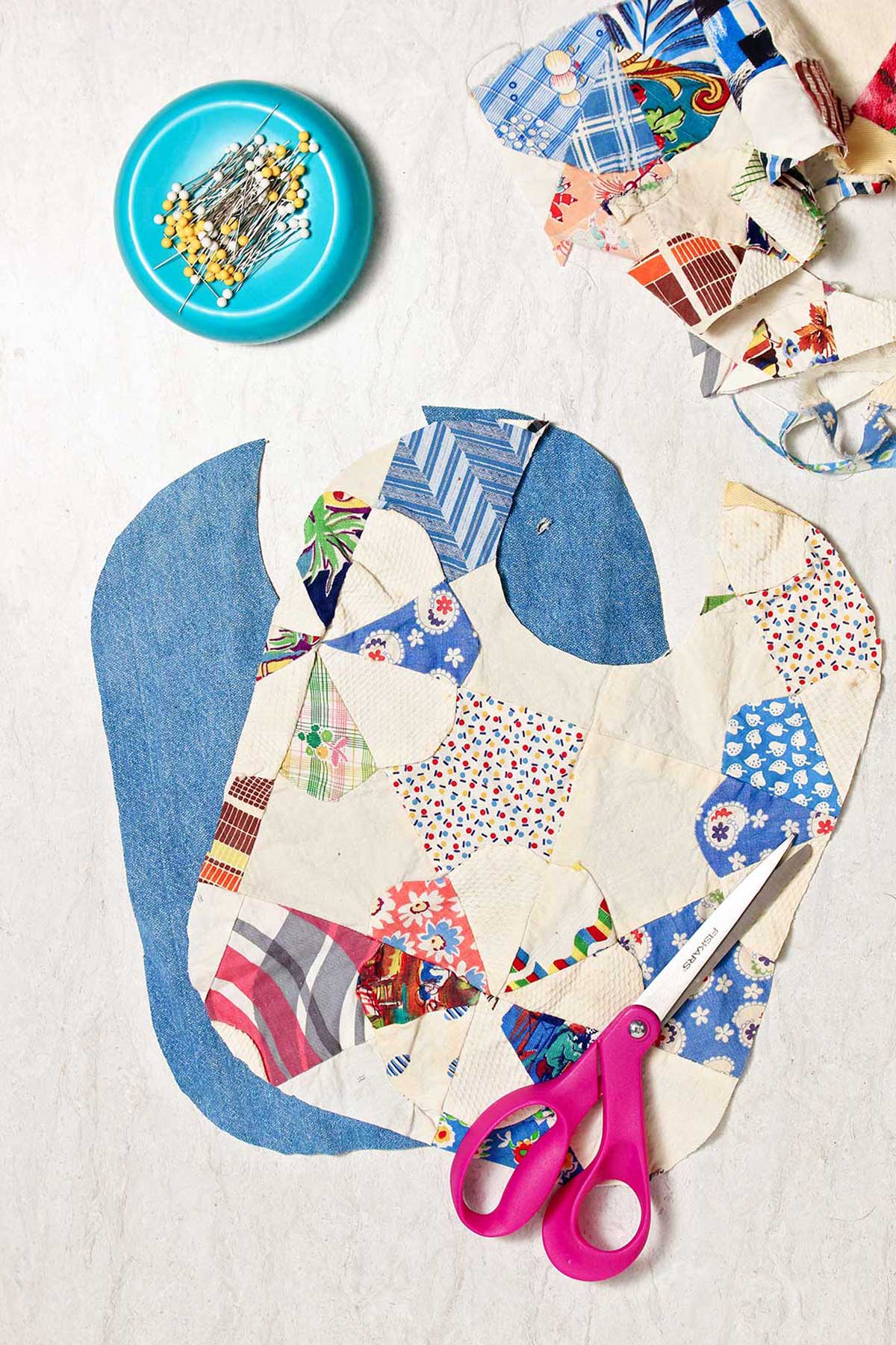 Two bib bases cut out of different fabric with pink scissors resting on top.