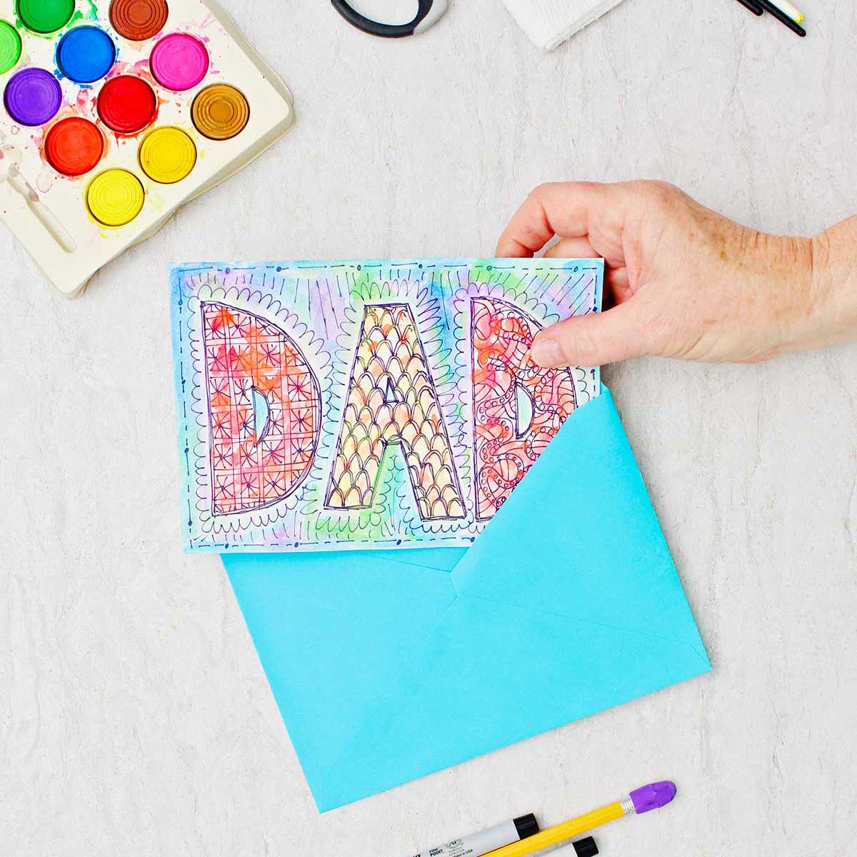 Doodle card for Dad made with watercolors and sharpie. Hand placing the card into a blue envelope.