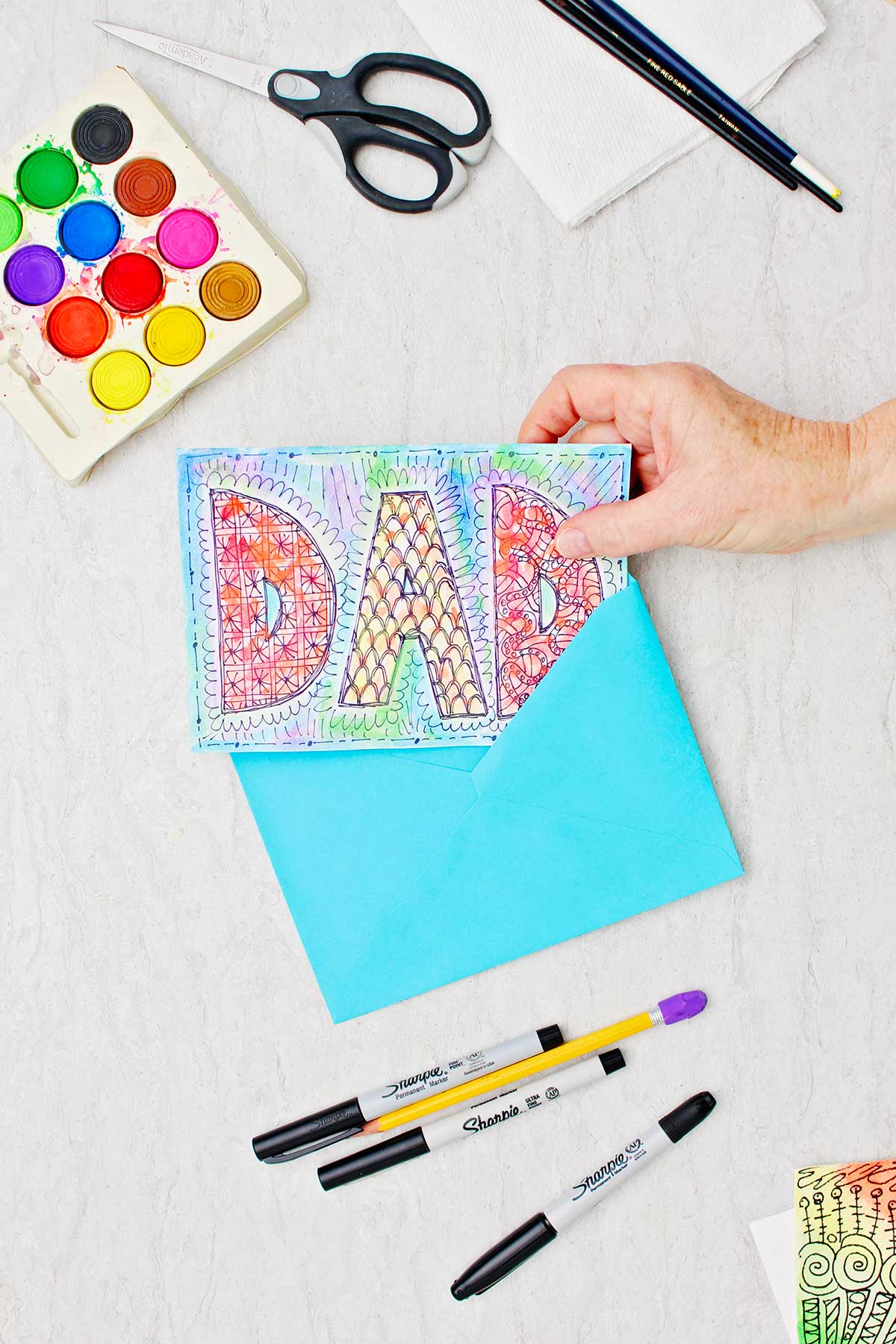 Doodle card for Dad made with watercolors and sharpie. Hand placing the card into a blue envelope.