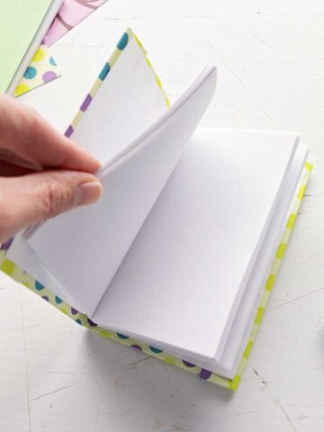 A DIY miniature journal with blank pages, scrapbook paper and pens in the background.