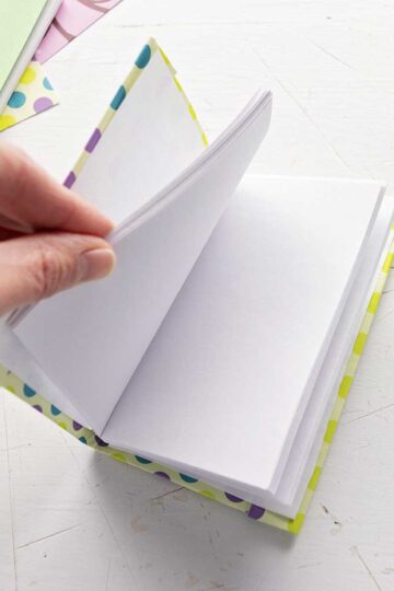 A DIY miniature journal with blank pages, scrapbook paper and pens in the background.