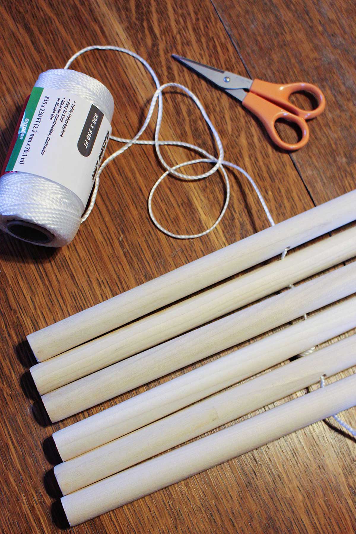 A roll of white cord running through some holes cut in wooden dowel rods with a pair of scissors nearby.