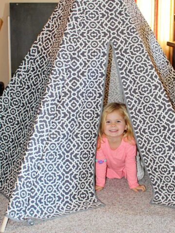 A little child inside a grey and white patterned fabric DIY teepee tent.