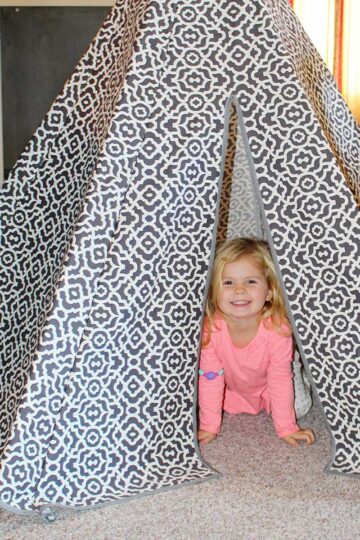 A little child inside a grey and white patterned fabric DIY teepee tent.