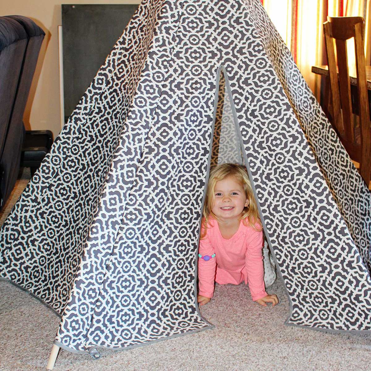 A little child inside a grey and white patterned fabric DIY teepee tent.