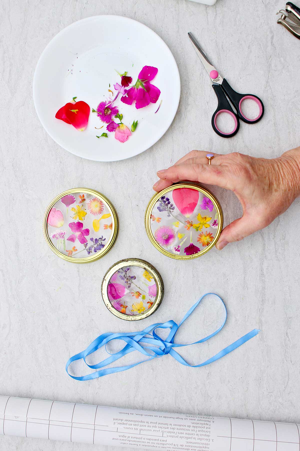 Person holding Garden Suncatcher before attaching blue ribbon for hanging with other supplies near by.