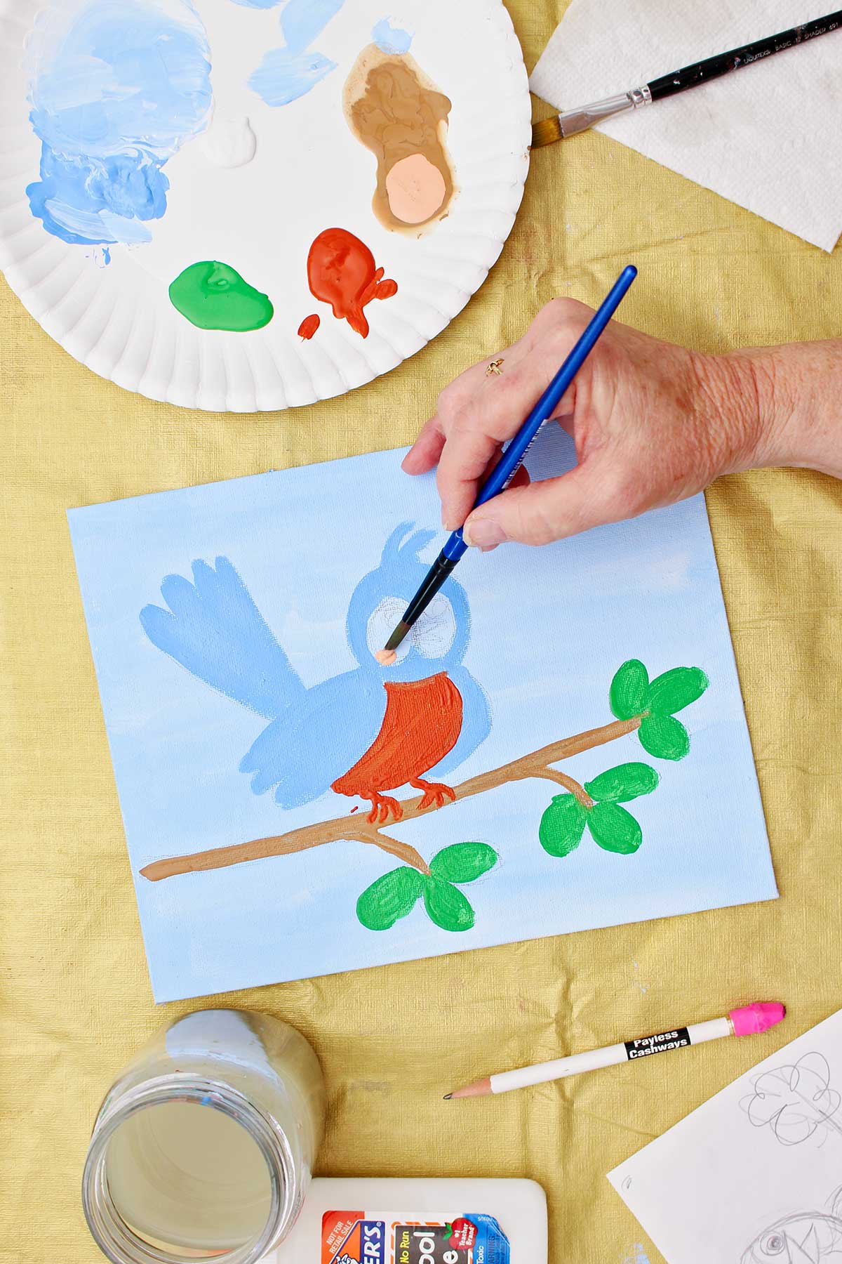 Person painting a bird sitting on a twig blue.