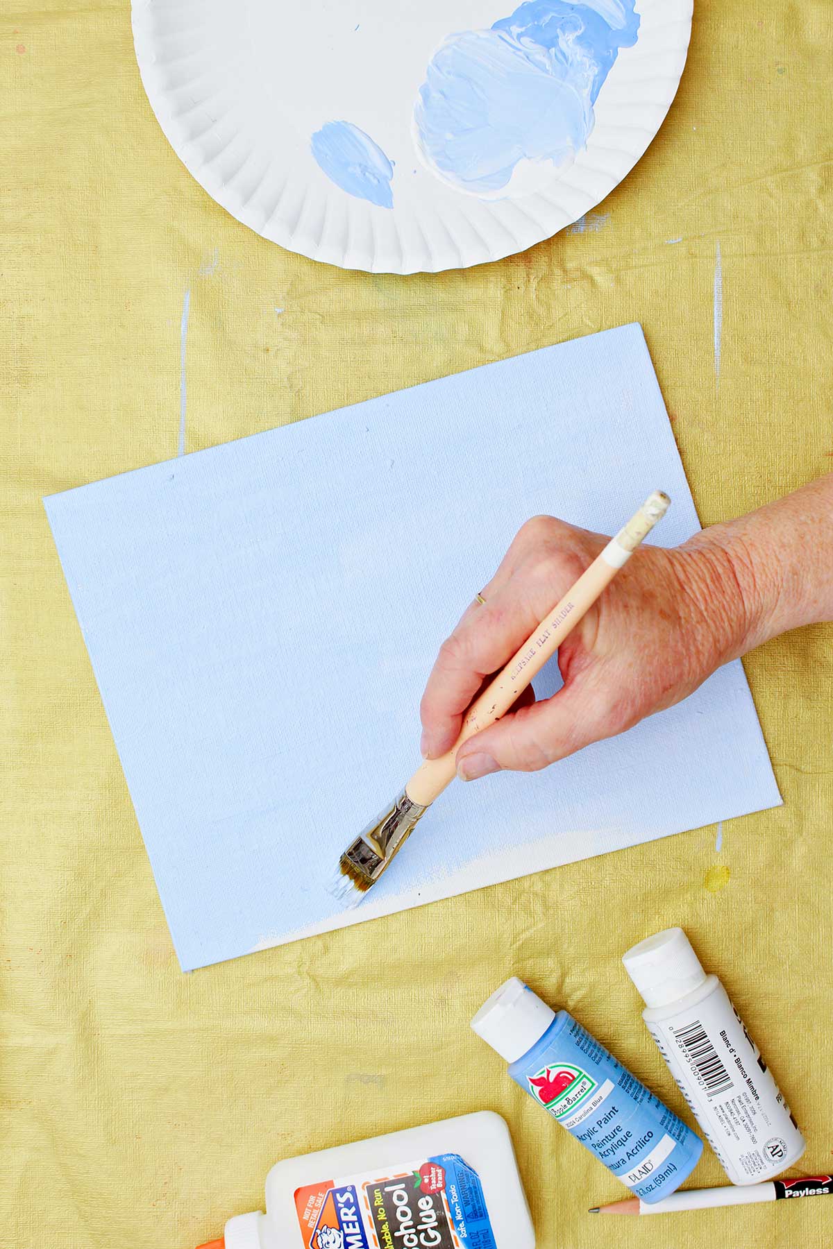 Person painting background of canvas light blue.