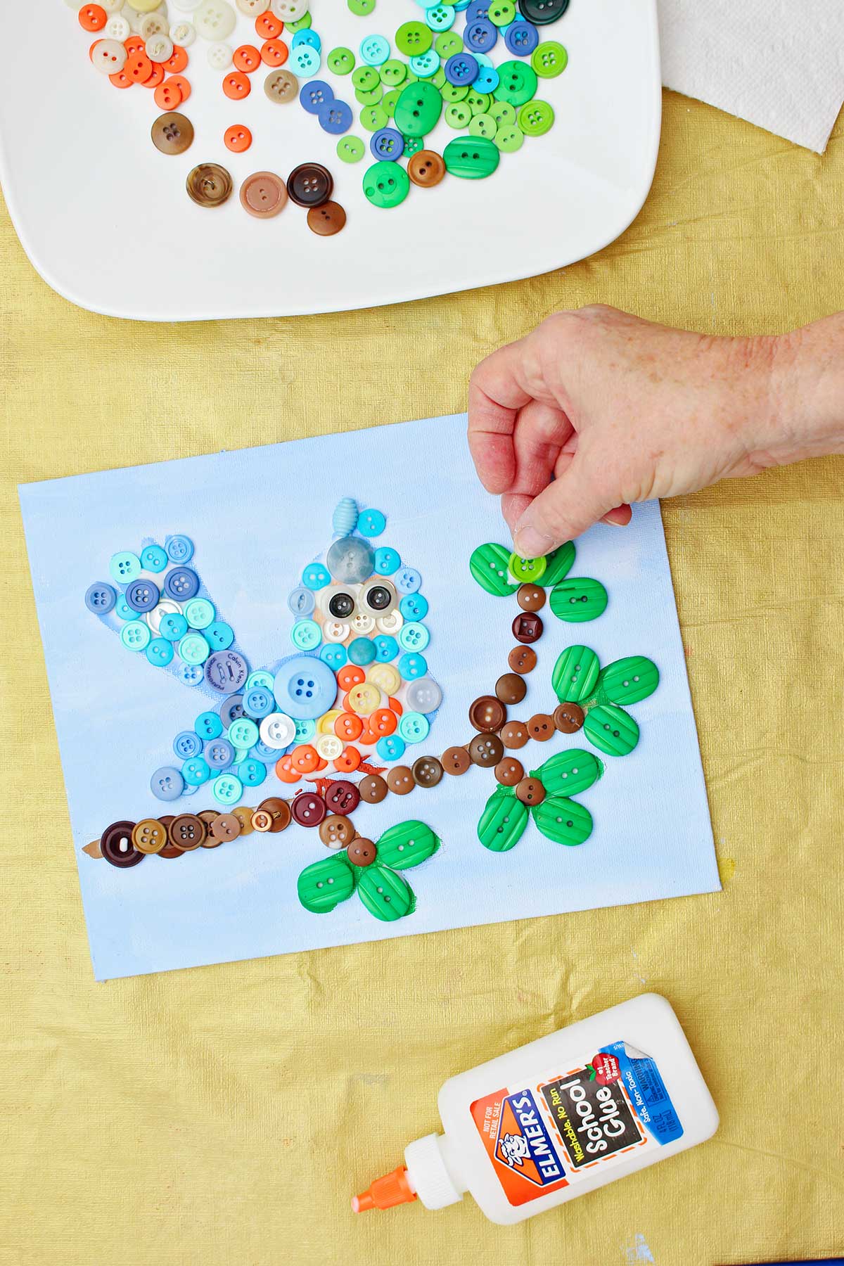 Person gluing green buttons to make leaves on button craft project.