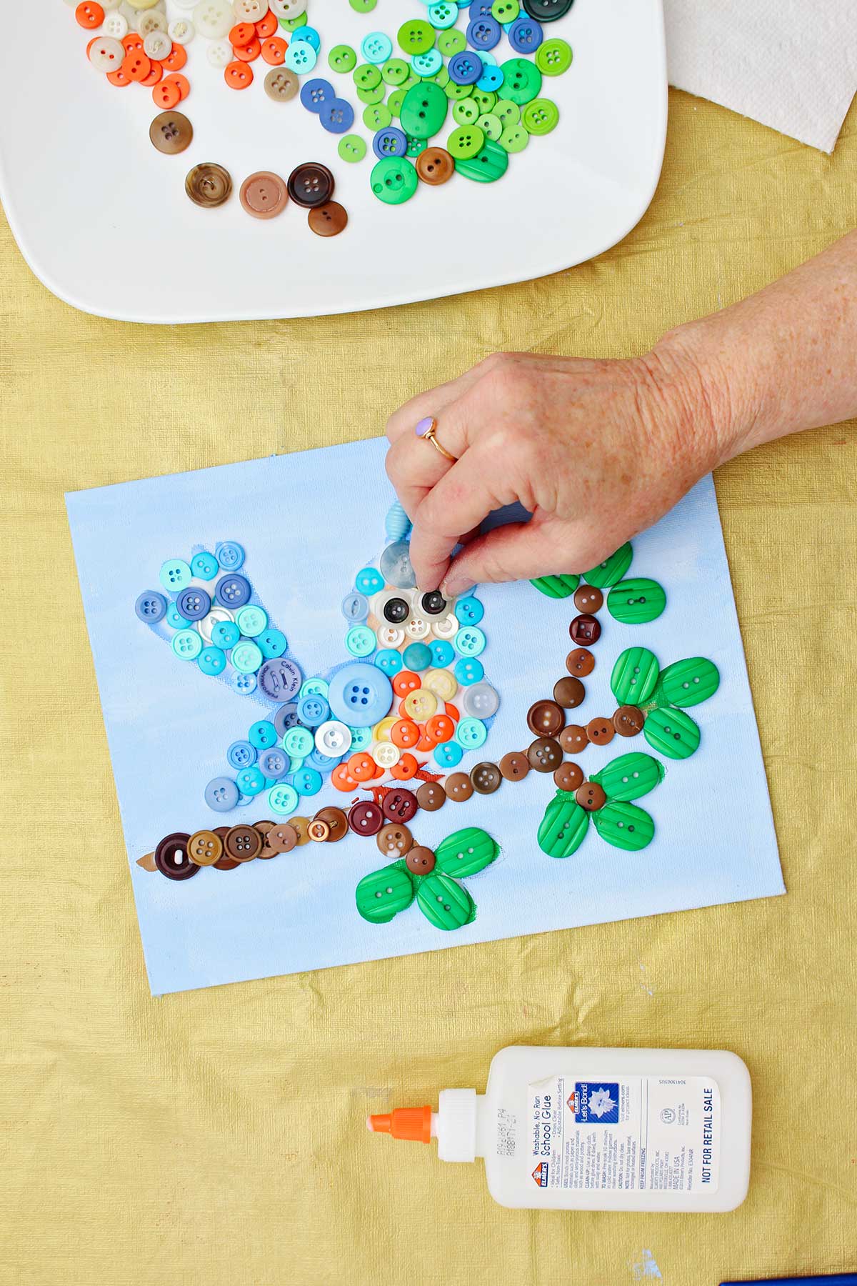 Person gluing black buttons to make eyes on button craft project.