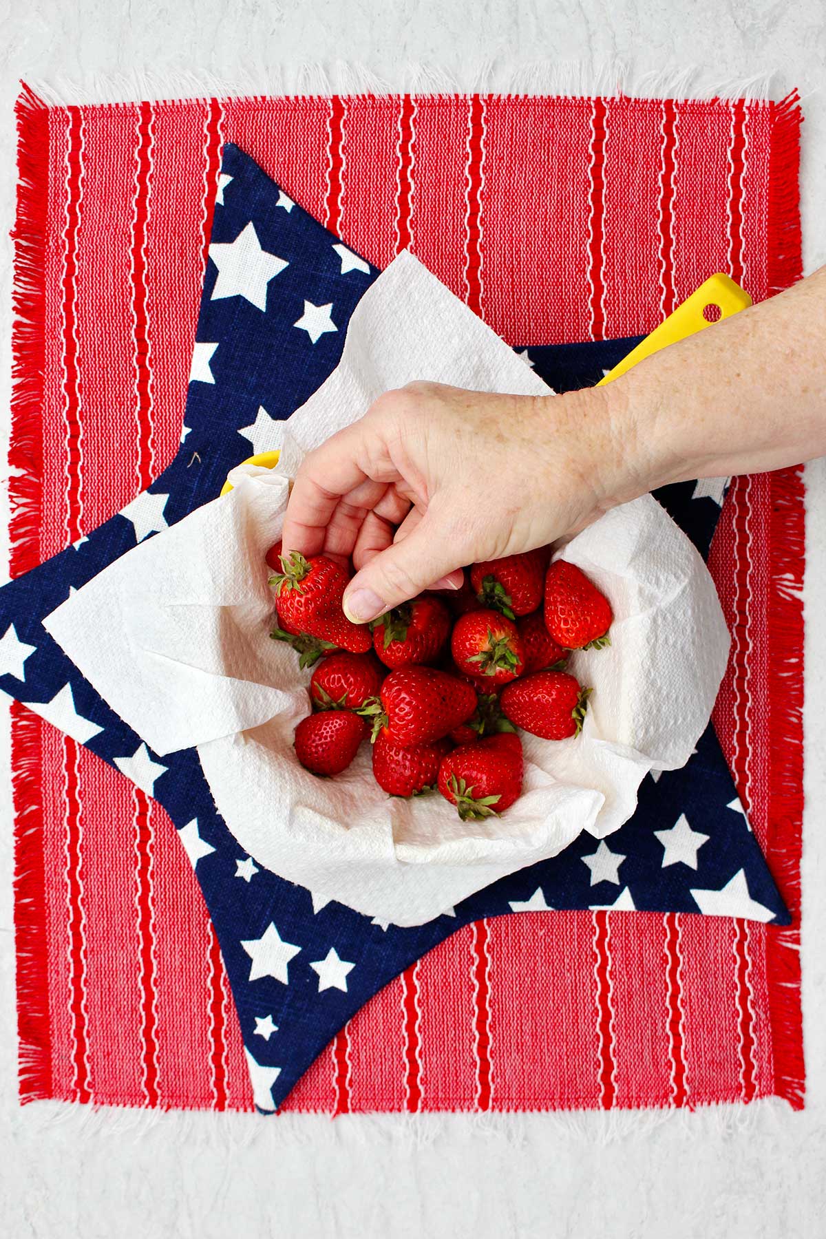 Person grabbing a strawberry out of bowl sitting on a red and star shaped placemat.