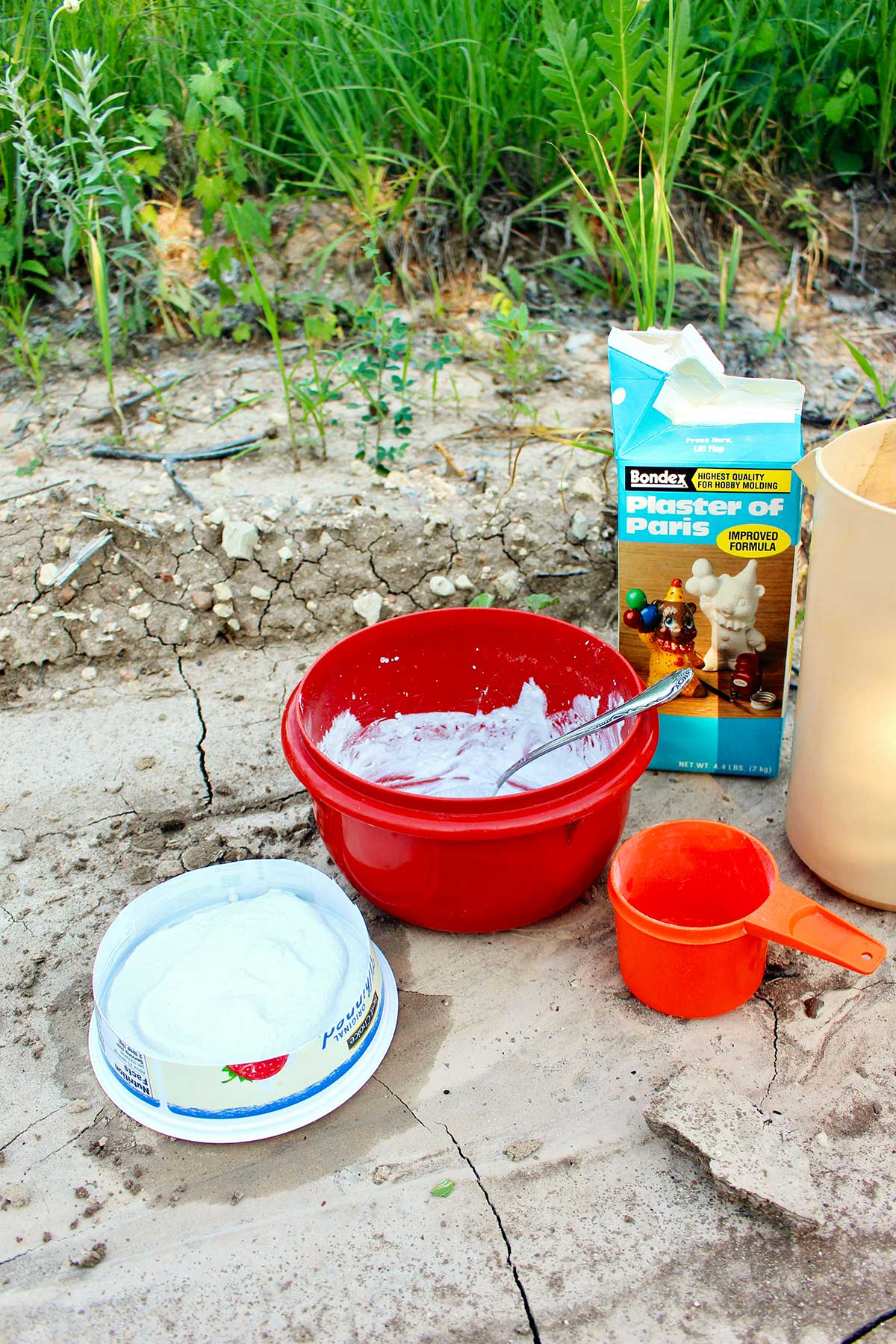 A bowl of plaster of Paris, a measuring cup and drying plaster cast of animal print outside.