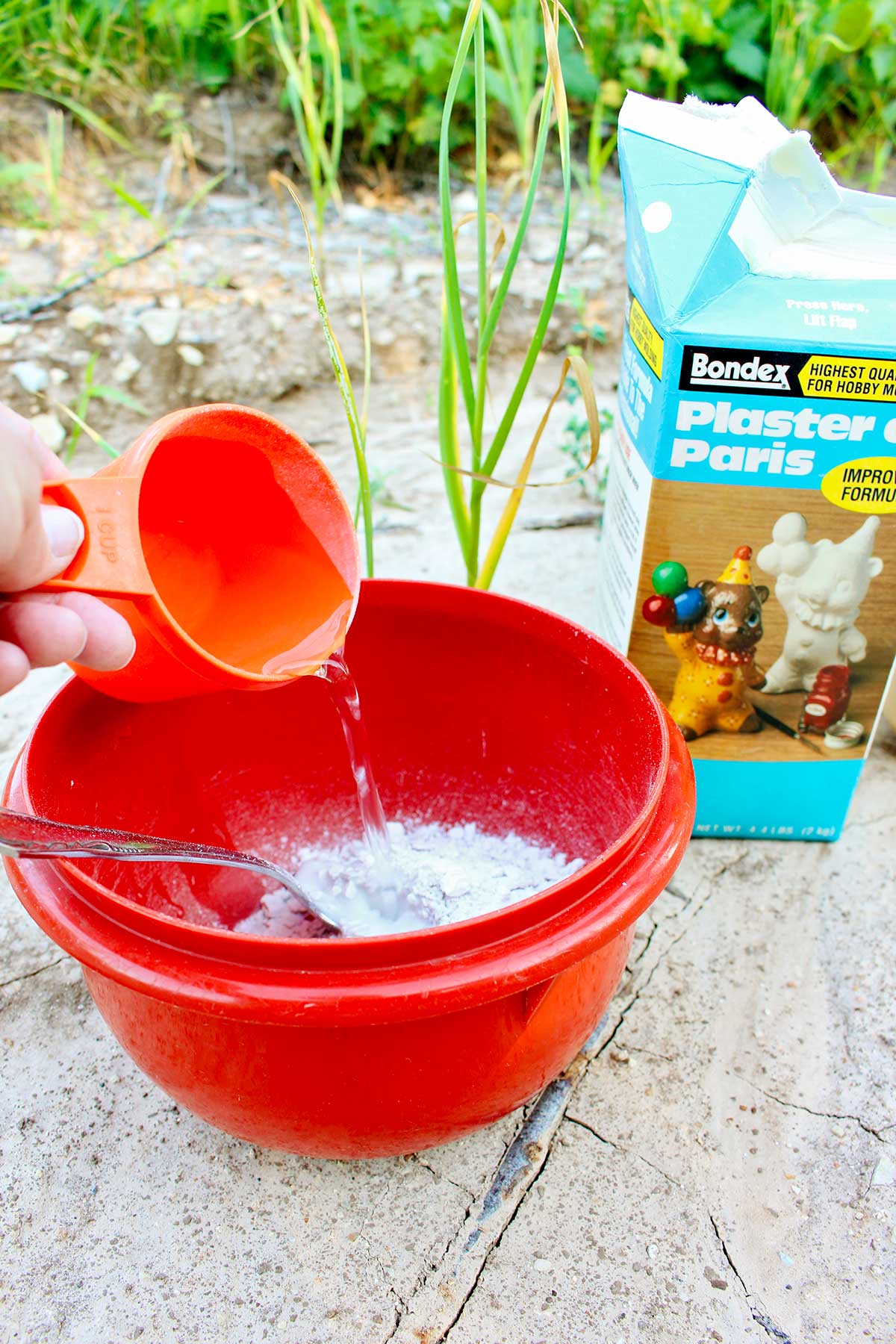 Person pouring water into a bowl of plaster of Paris outside.