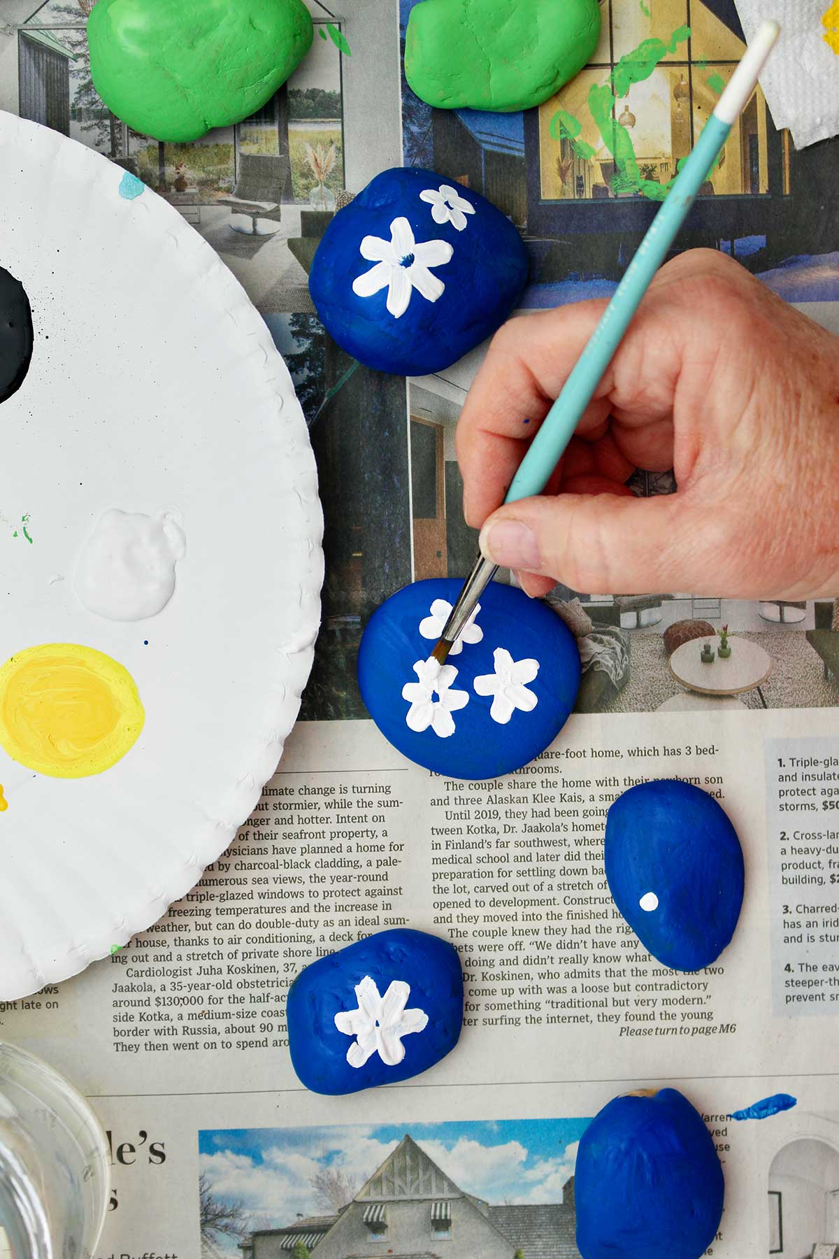 Person painting white flowers on a blue rock.