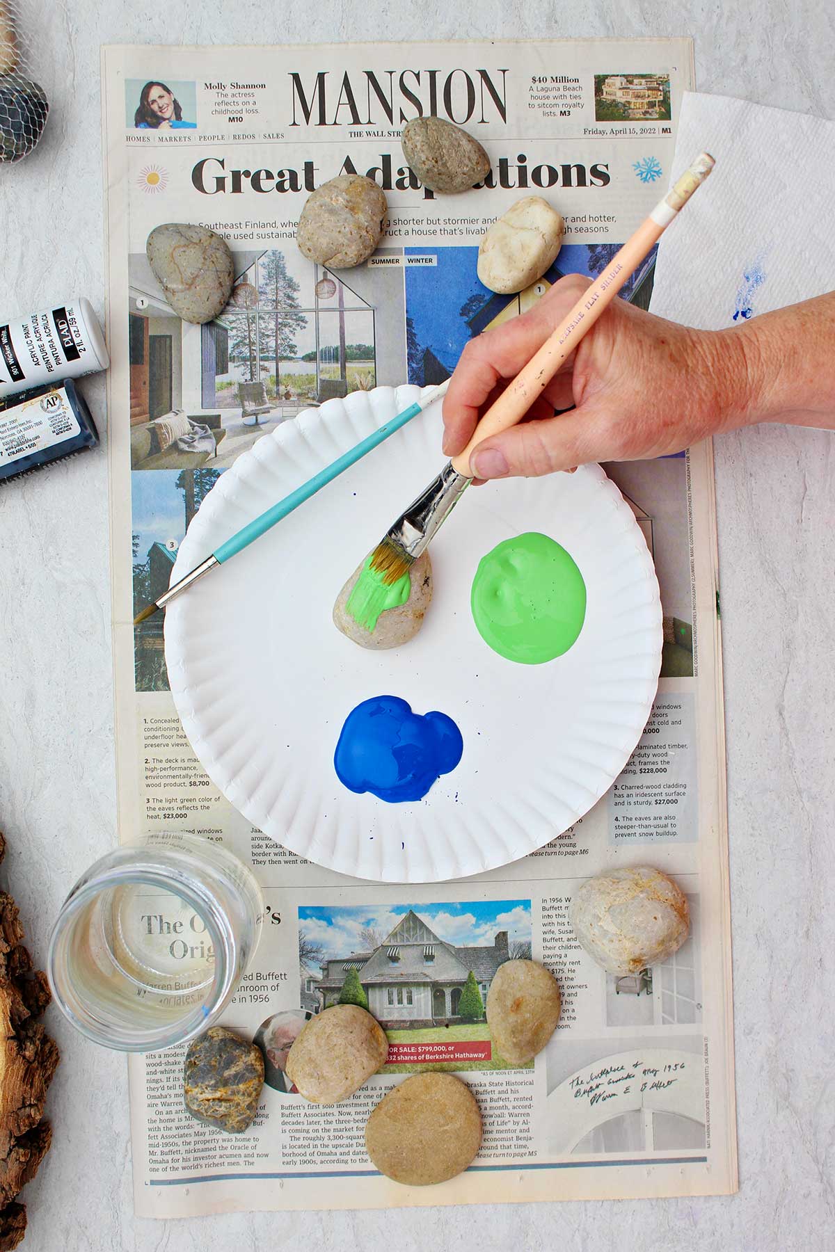 Person painting rock green with other rocks and supplies near by.