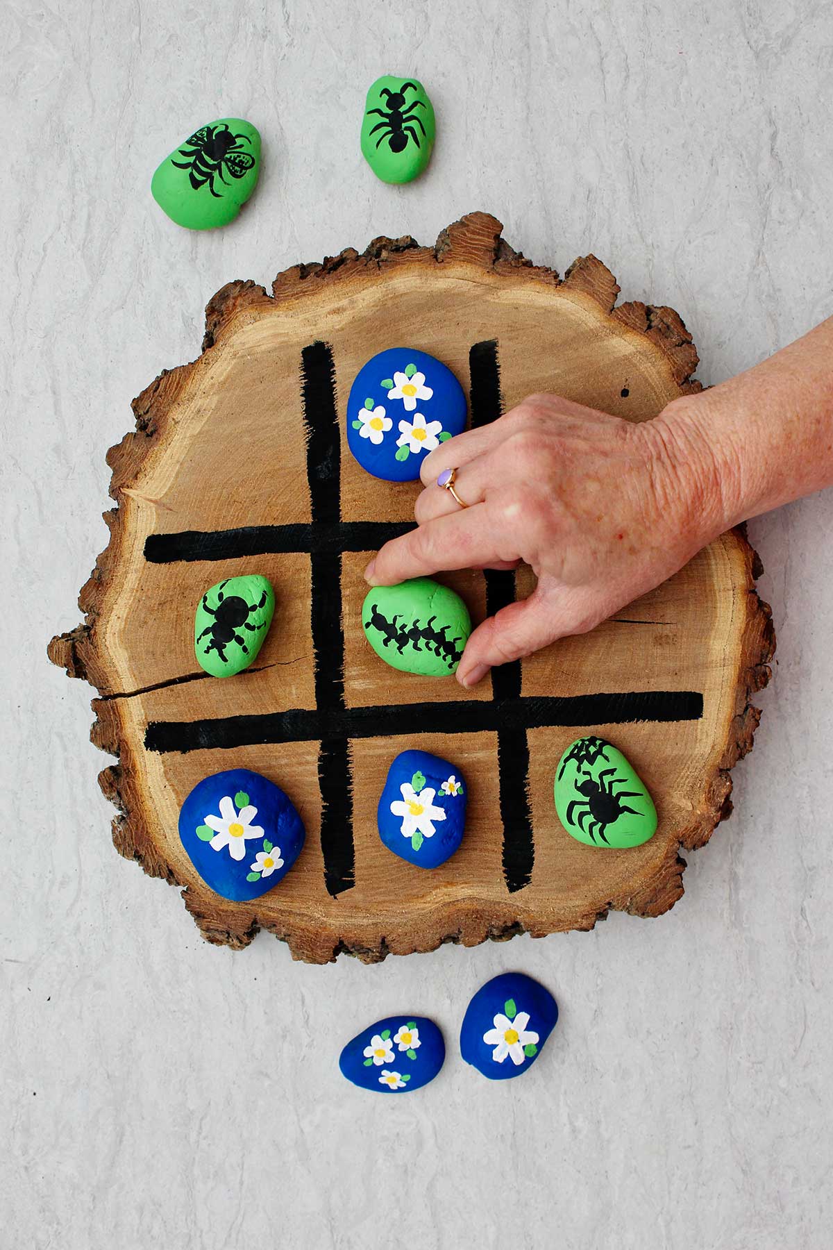 Person playing tic tac toe on wooden board moving a green bug rock.