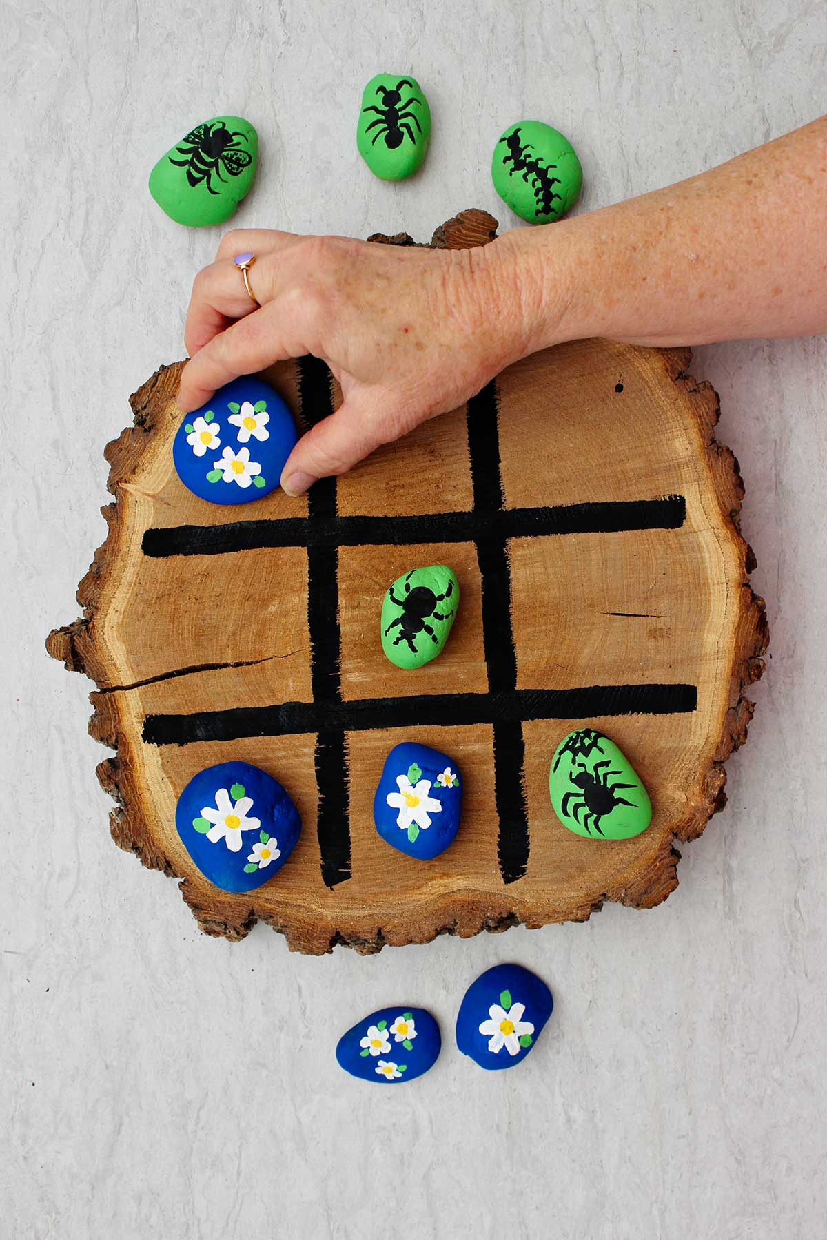 Person playing tic tac toe on wooden board moving a blue flower rock.