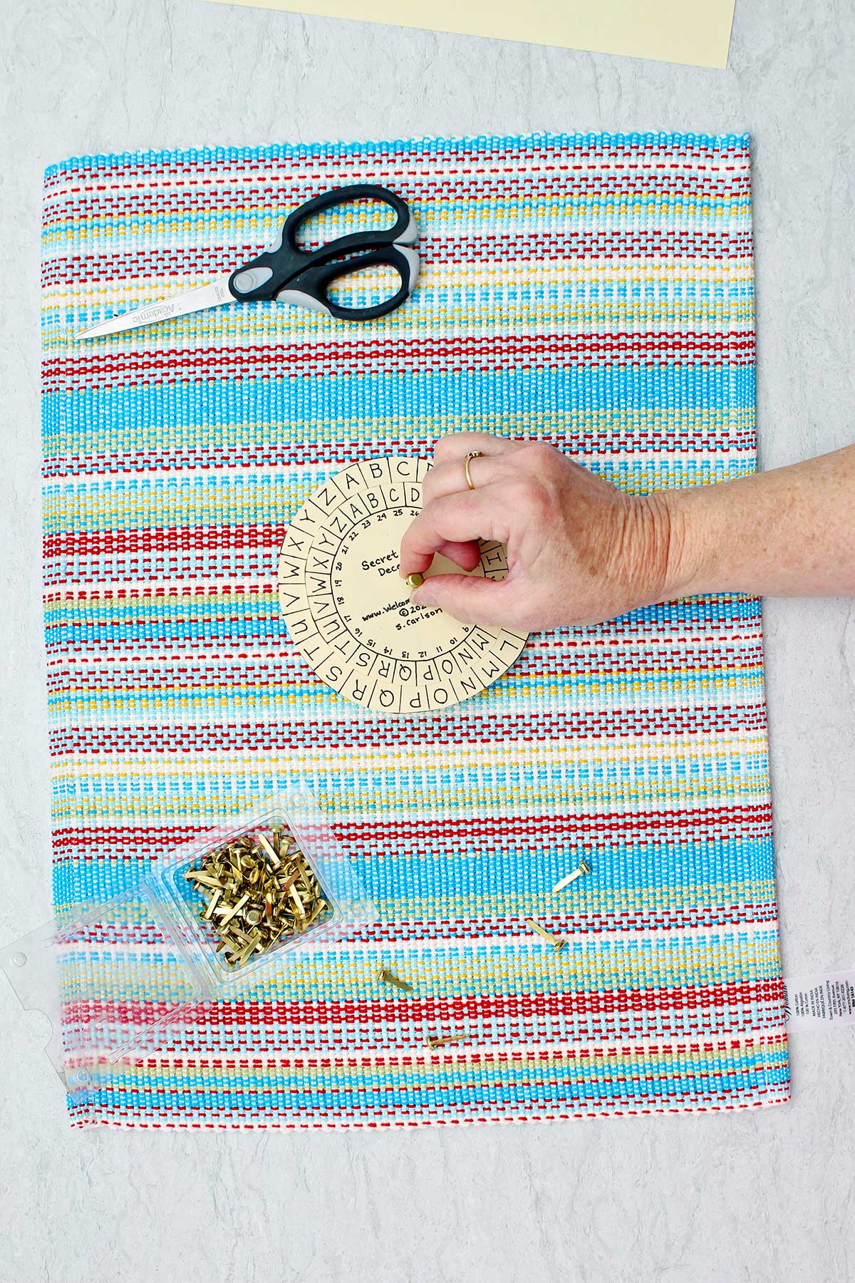 Person placing brass brad in the center of the two decoder cut outs with scissors and brass brads near by.