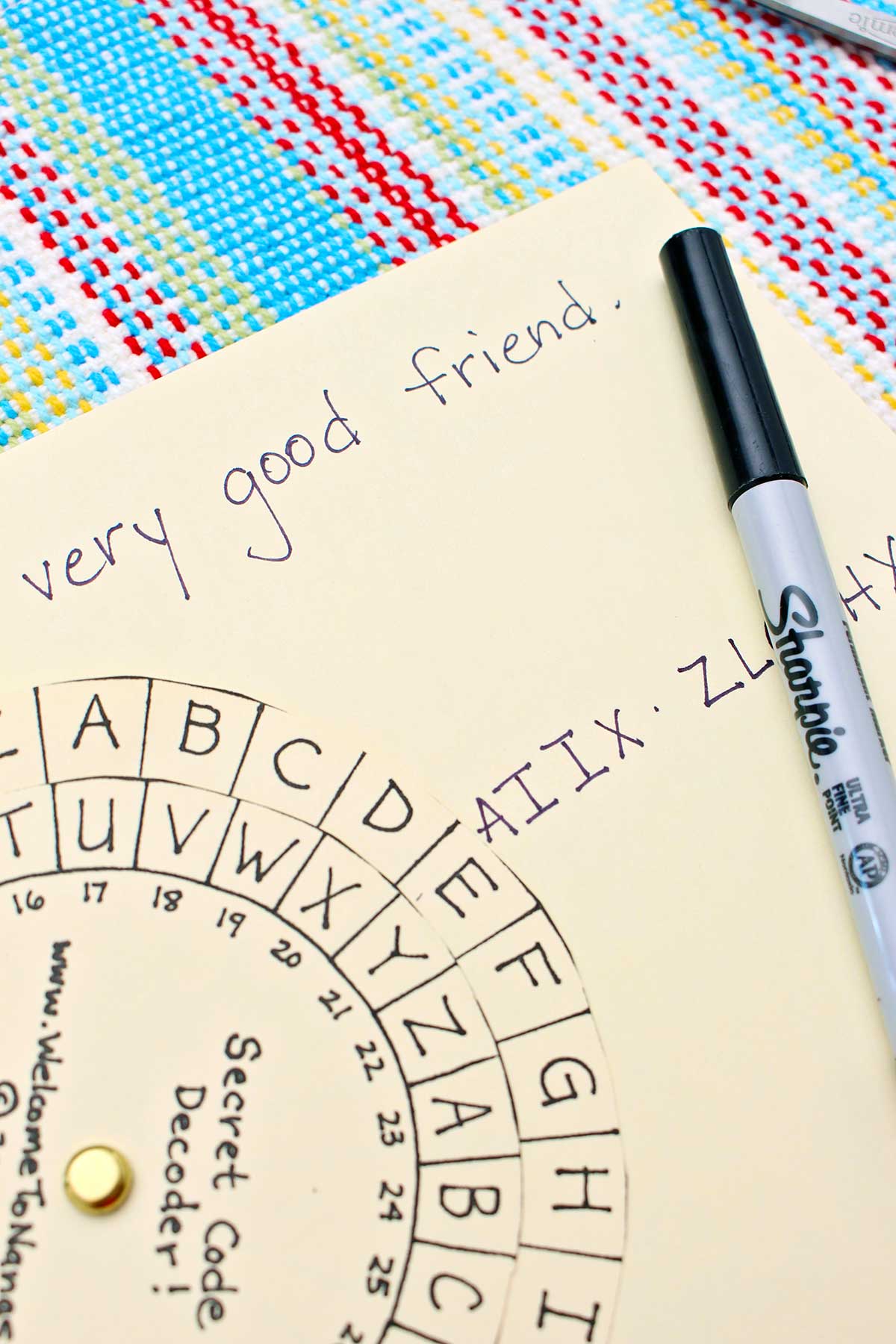 Close up view of the secret message decoder, the secret message and a sharpie marker on a colorful place mat.