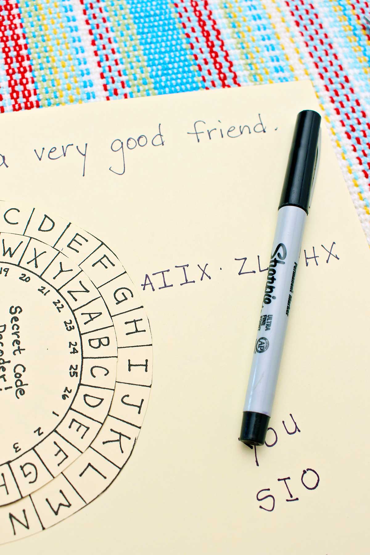 Close up view of the secret message decoder, the secret message and a sharpie marker on a colorful place mat.