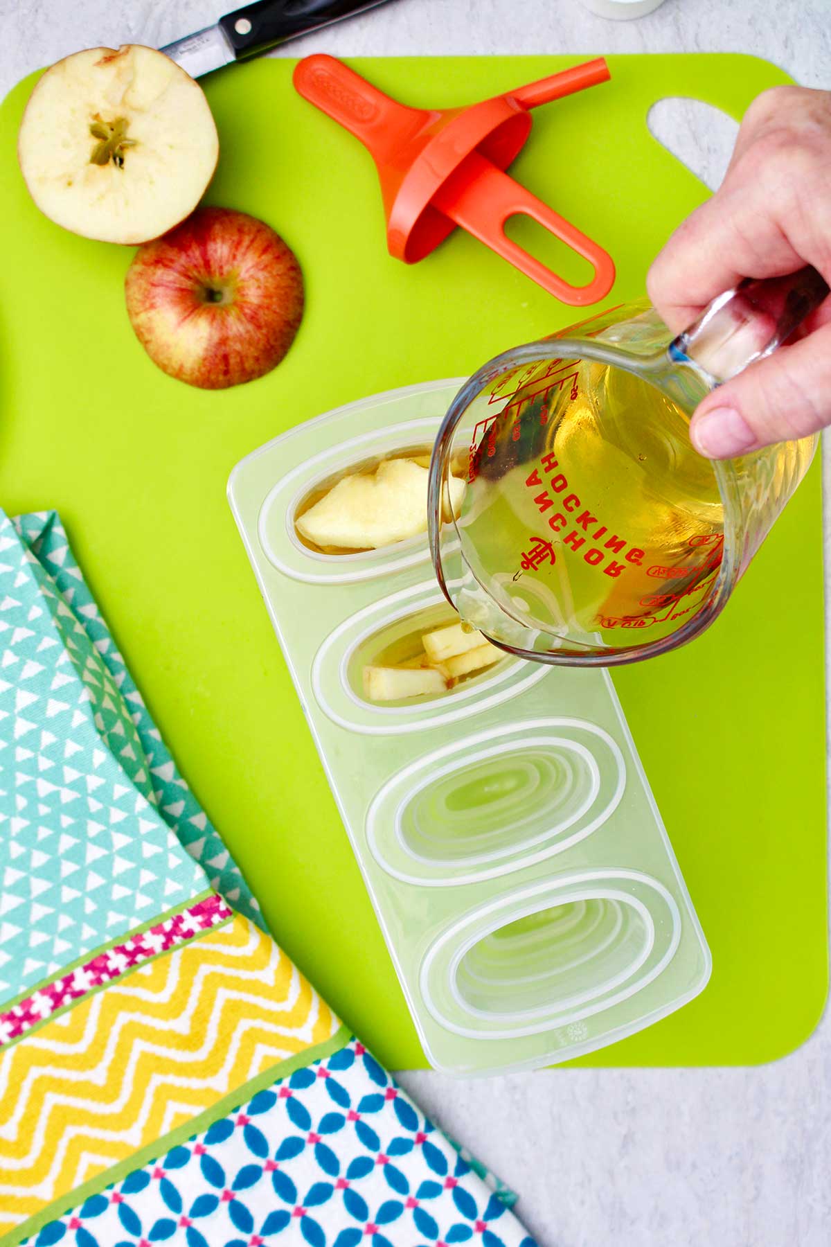 Person pouring apple juice into popsicle molds with slices of apples in them.