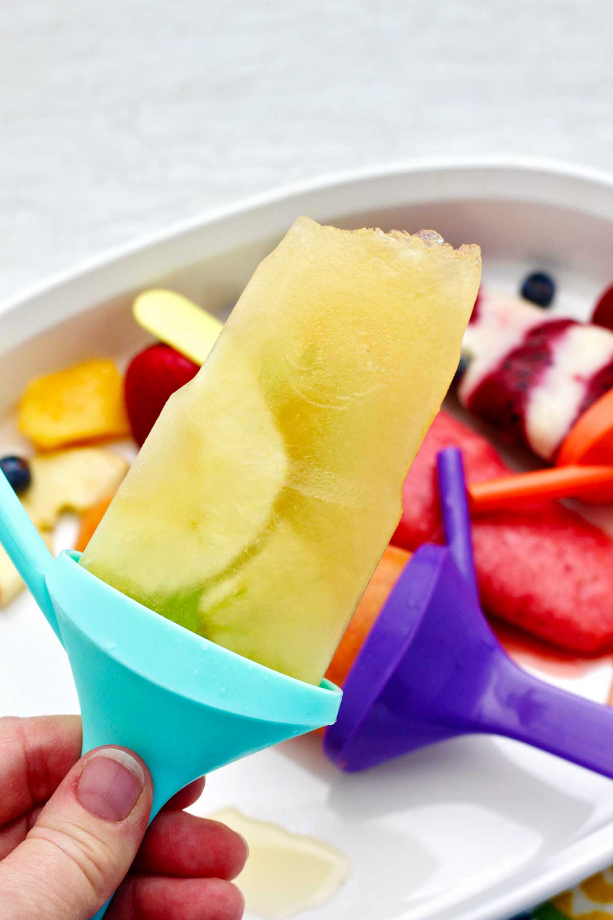 Person holding an apple flavored popsicle on an aqua popsicle holder.