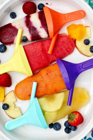 Four different flavored popsicles on colorful popsicle handles resting on a platter of fruit.