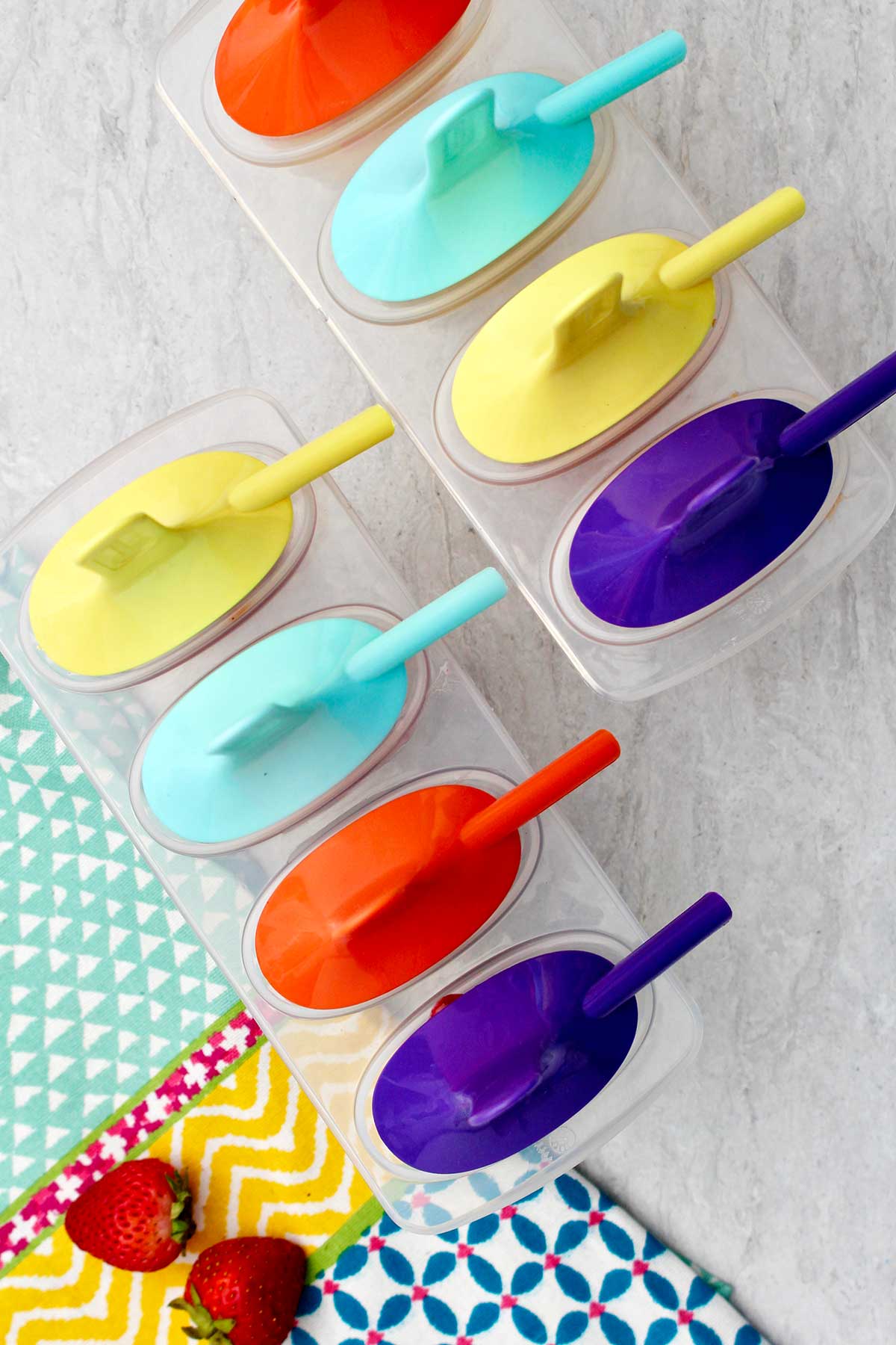 Two trays of popsicles with colorful holders ready to go in the freezer.