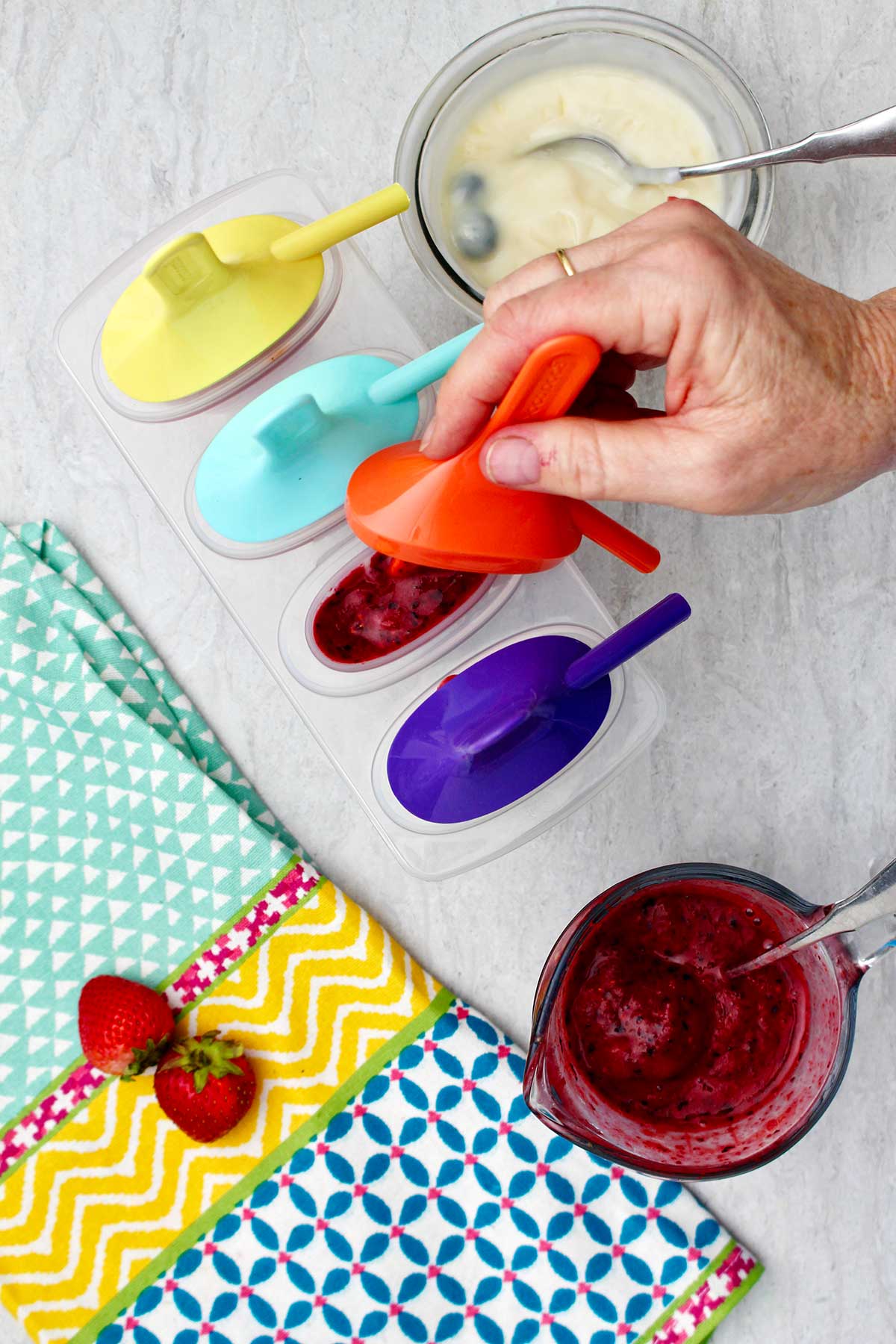 Person placing orange popsicle holder inside a blueberry flavored popsicle.