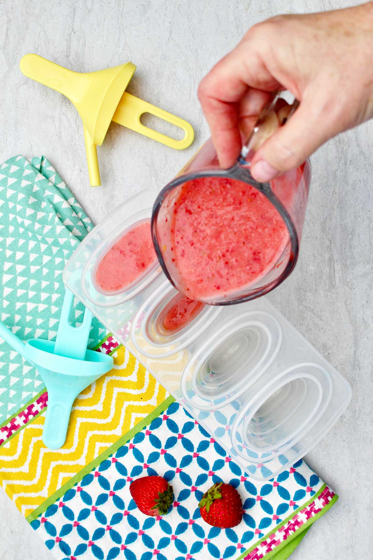 Person pouring strawberry puree into popsicle molds.