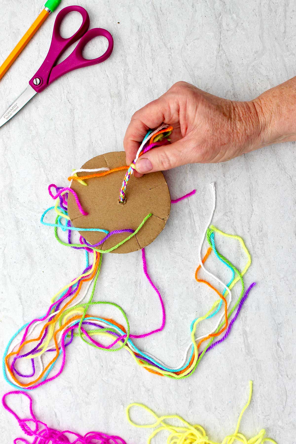 Person showing the beginnings of a round friendship bracelet, still on the cardboard loom.