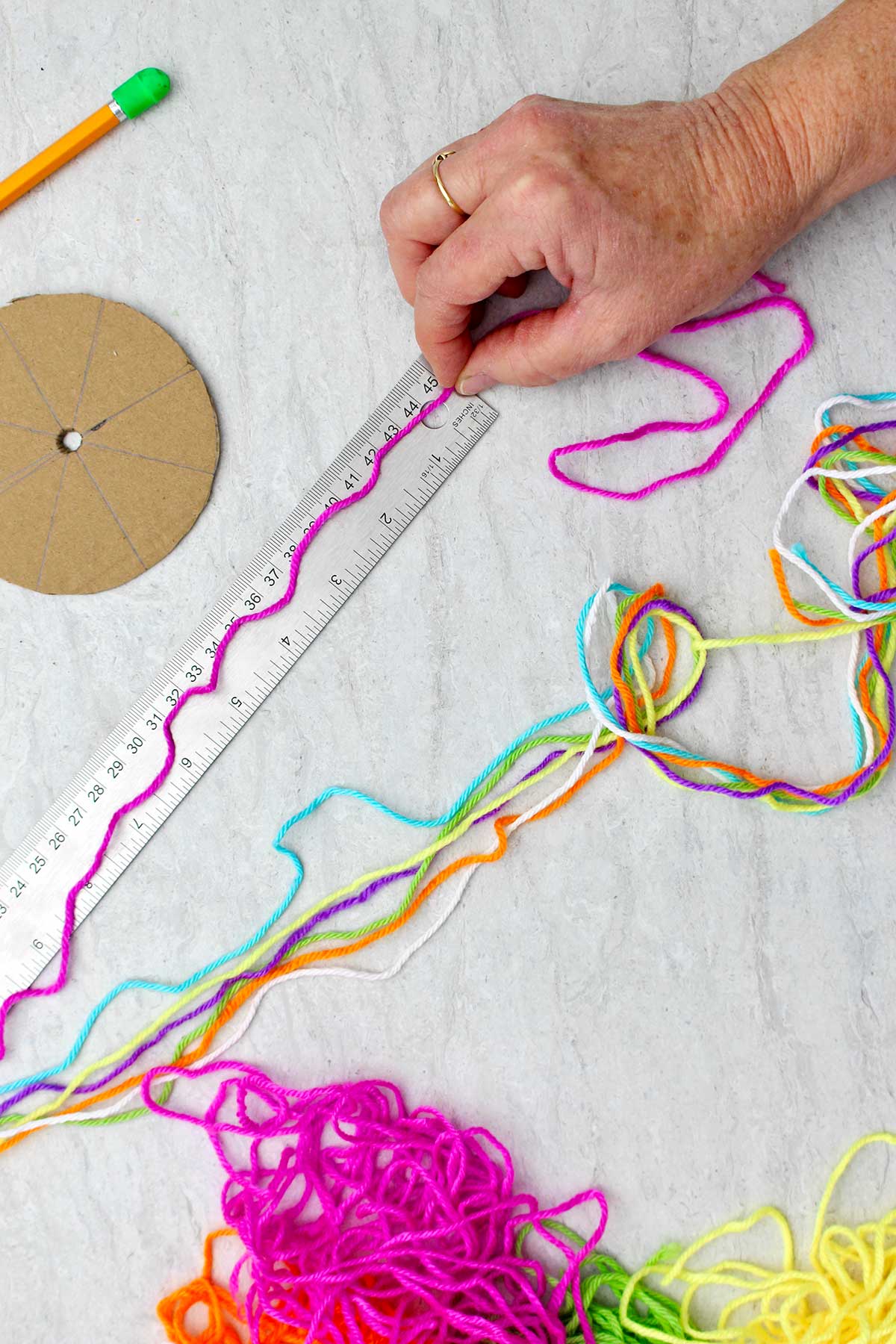 Person measuring a piece of magenta yarn with other colorful pieces of yarn near by.