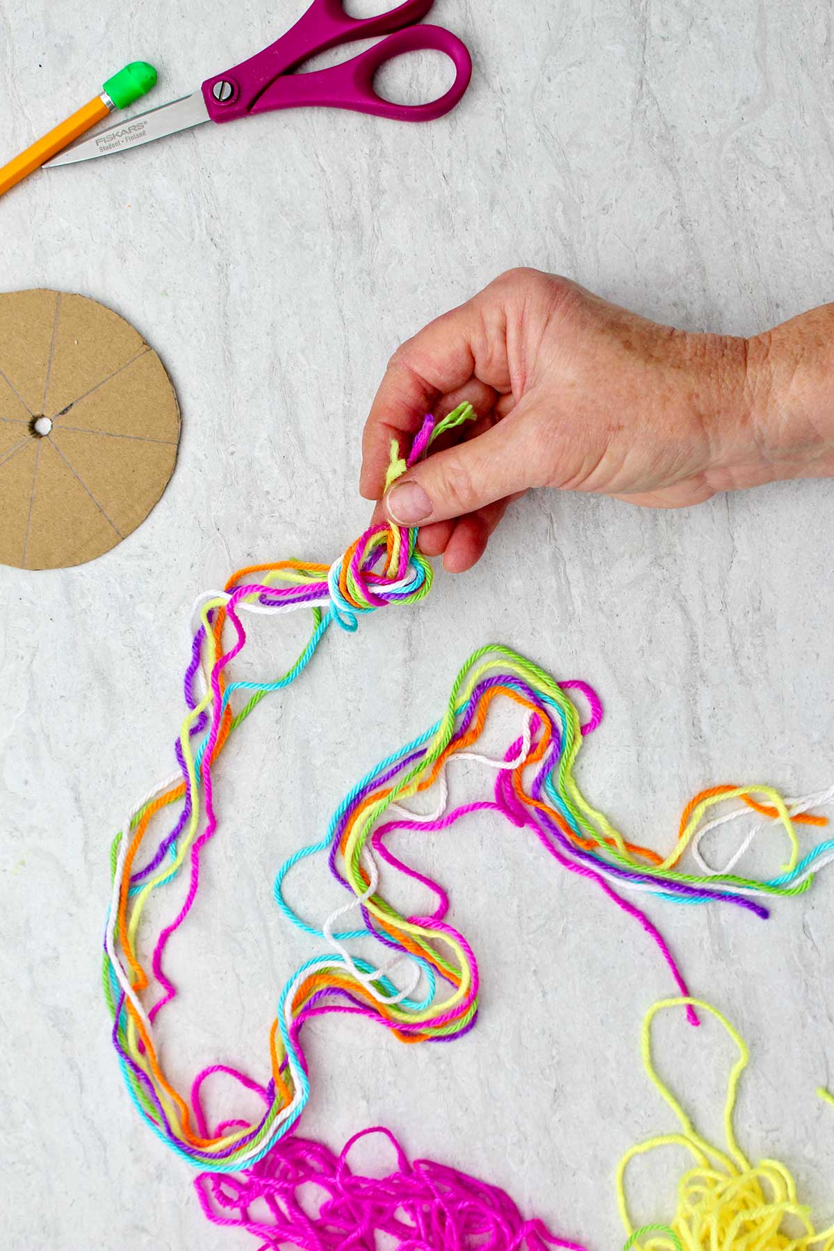 Person tying a knot in six different colored pieces of yarn.