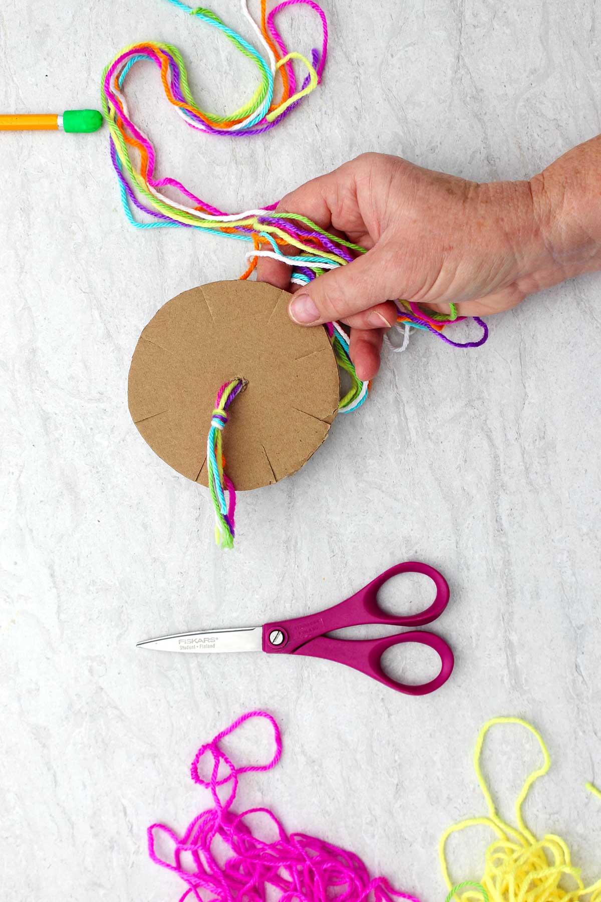 Underside of cardboard loom with tied off bundle of colorful yarn.