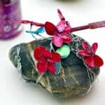 Person painting pink glittery nail polish on pink nail polish flowers.
