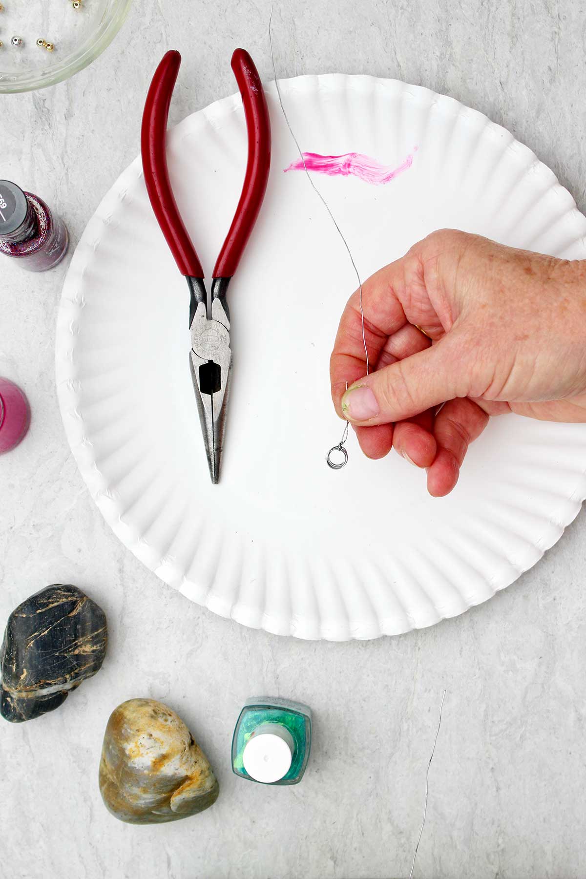 Person holding wire twisted in the shape of a small circle with other supplies near by.