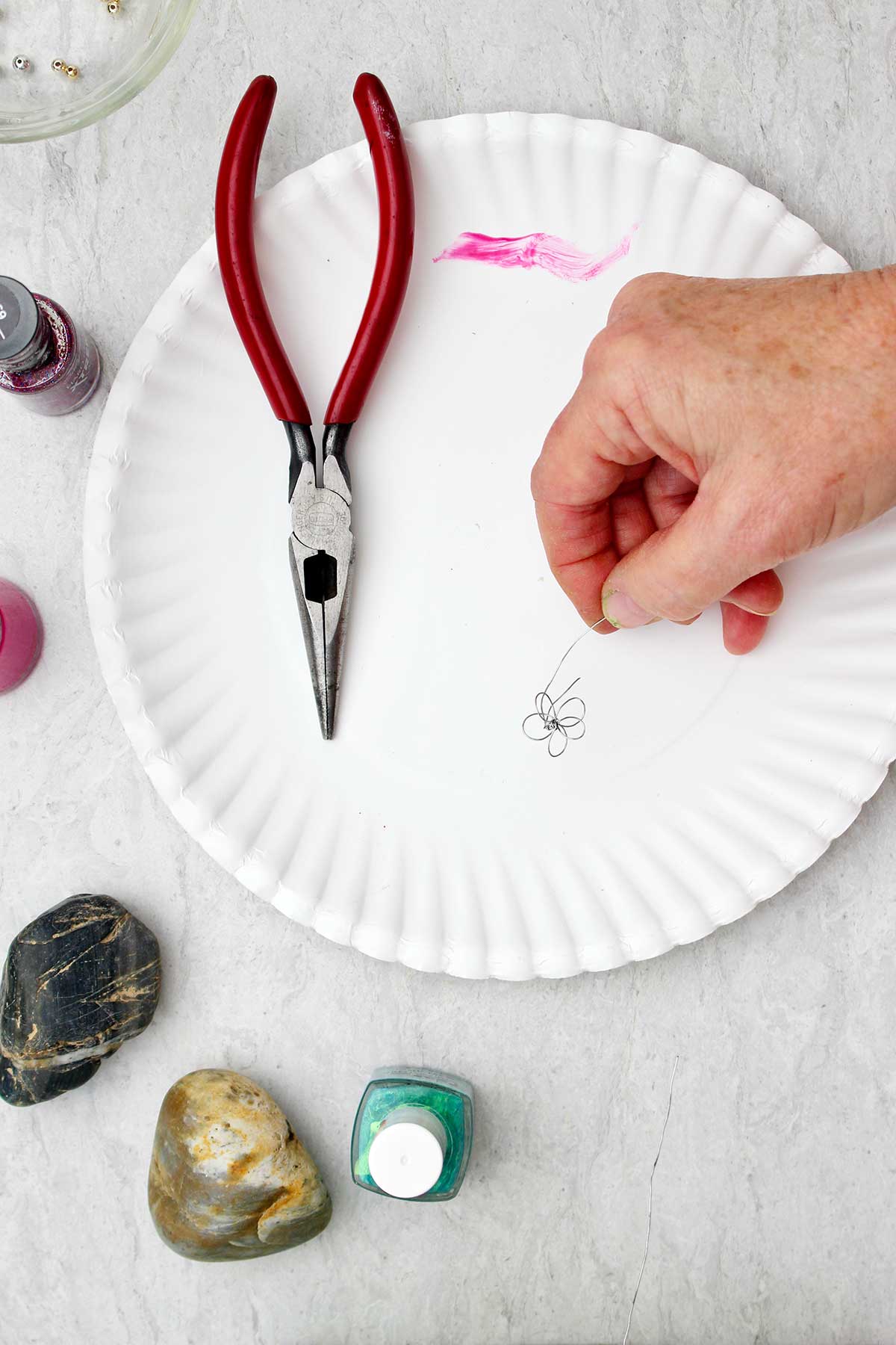 Person holding wire twisted in the shape of a flower with other supplies near by.