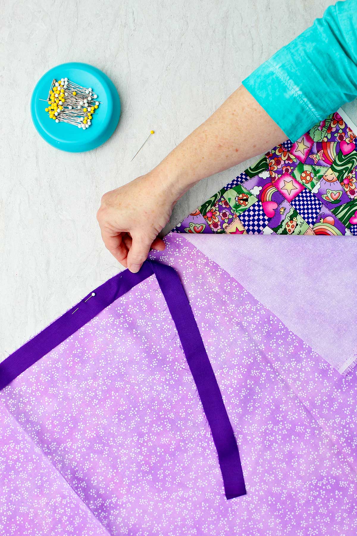 Person pinning dark purple strip of fabric along the right side of purple fabric.