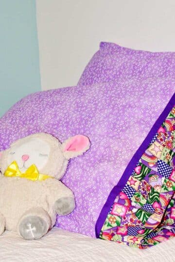 Completed pillowcases made with purple patterned fabric with stuffed animal lamb resting against them.