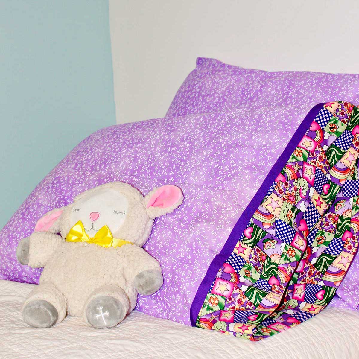 Completed pillowcases made with purple patterned fabric with stuffed animal lamb resting against them.