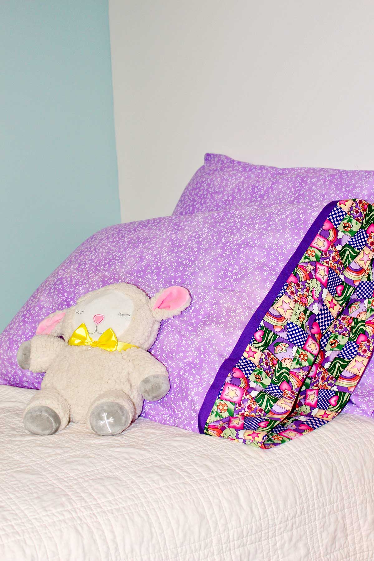 Completed pillowcases made with purple patterned fabric with stuffed animal lamb resting against them.