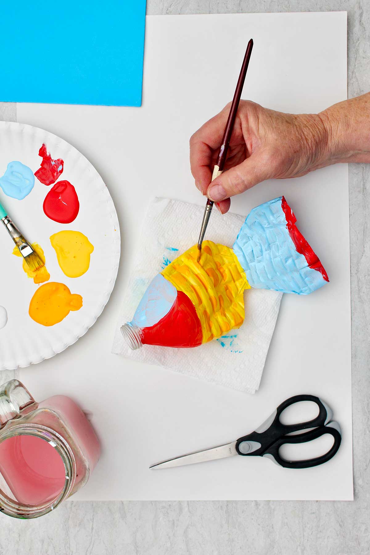 Person painting middle part of water bottle yellow and red for scales with other supplies near by.