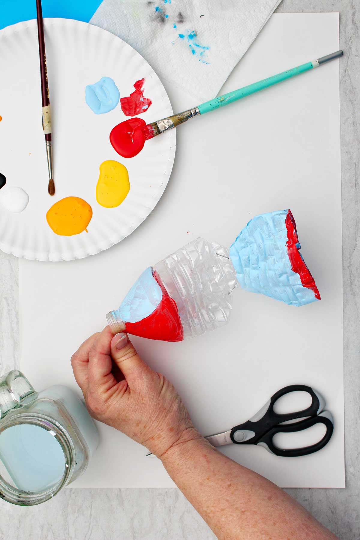 Person holding water bottle to paint with other supplies near by.