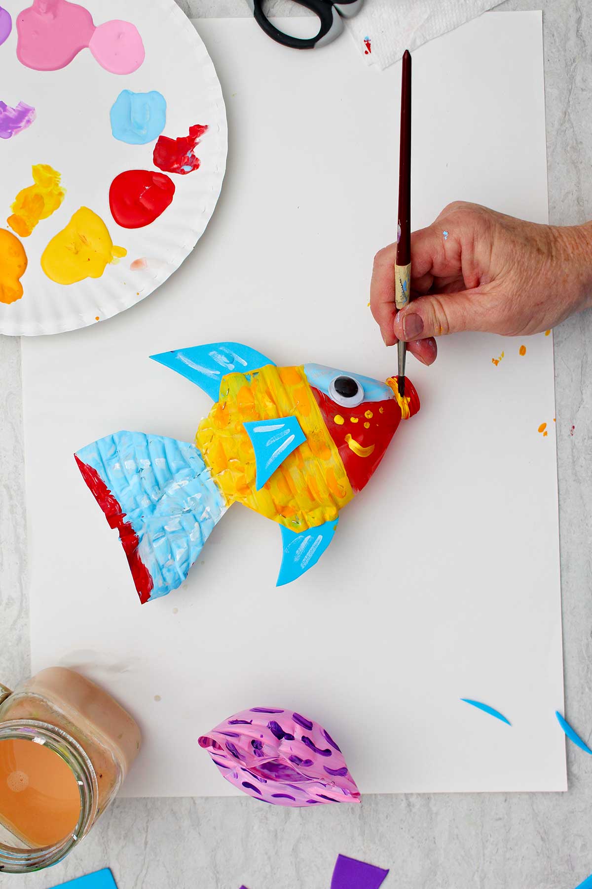 Person painting mouthpiece of water bottle red in completed plastic bottle fish.