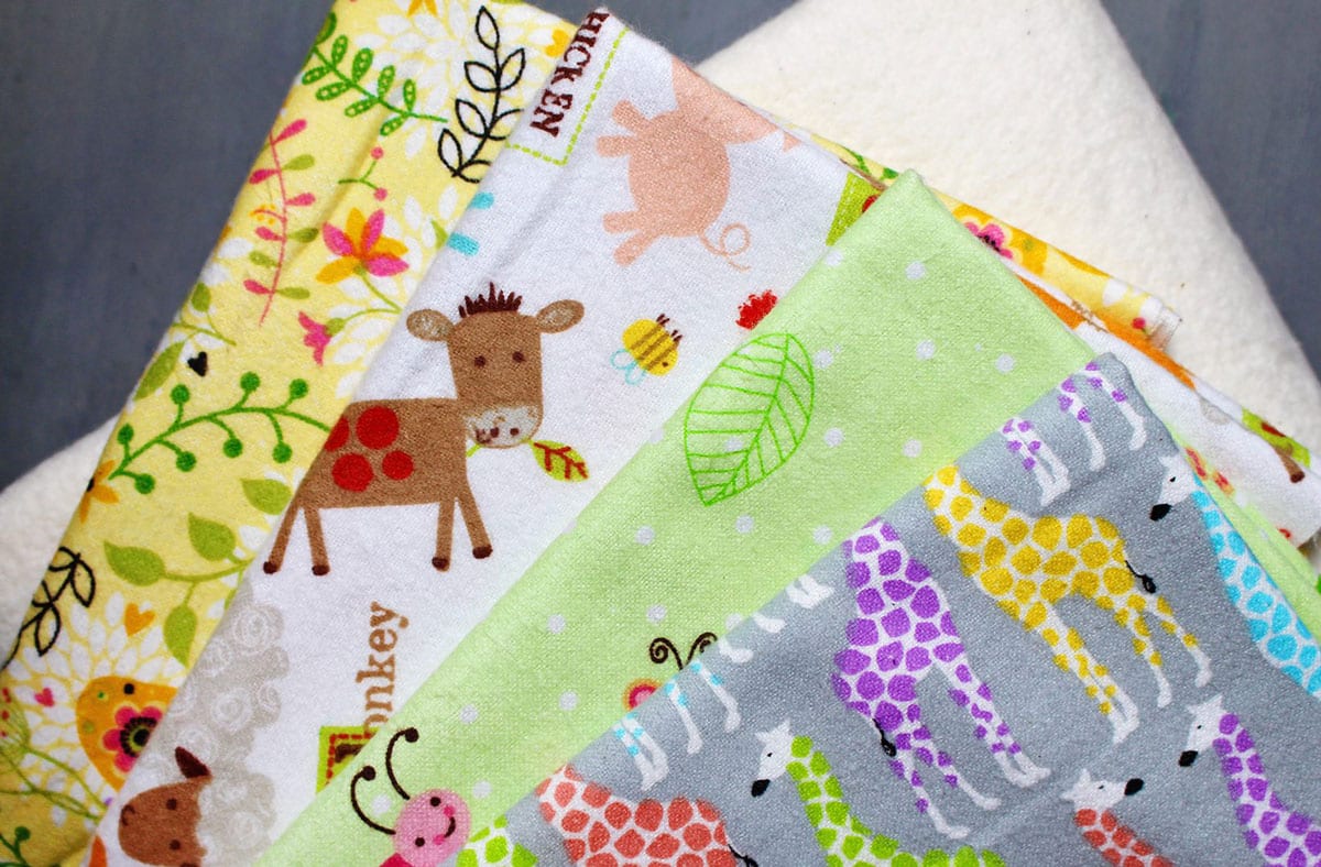 A stack of brightly colored felt fabric prints ready to be sewed into baby burp cloths.