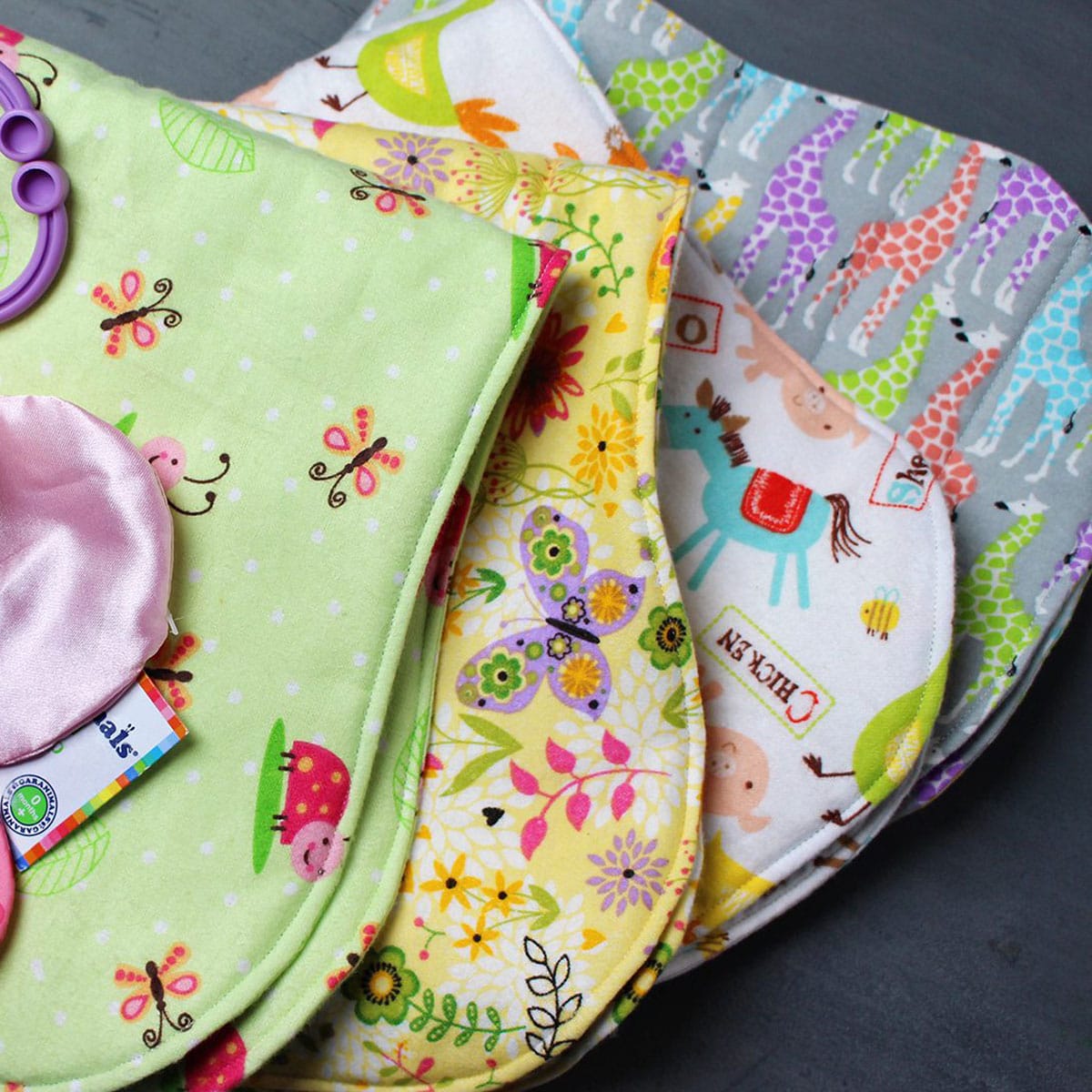 A stack of baby burp cloths made from brightly colored felt fabric prints.