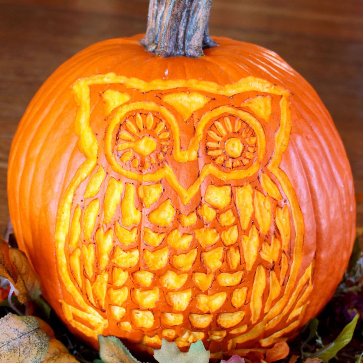 A woodland owl carved pumpkin sitting with some fall leaves on a table