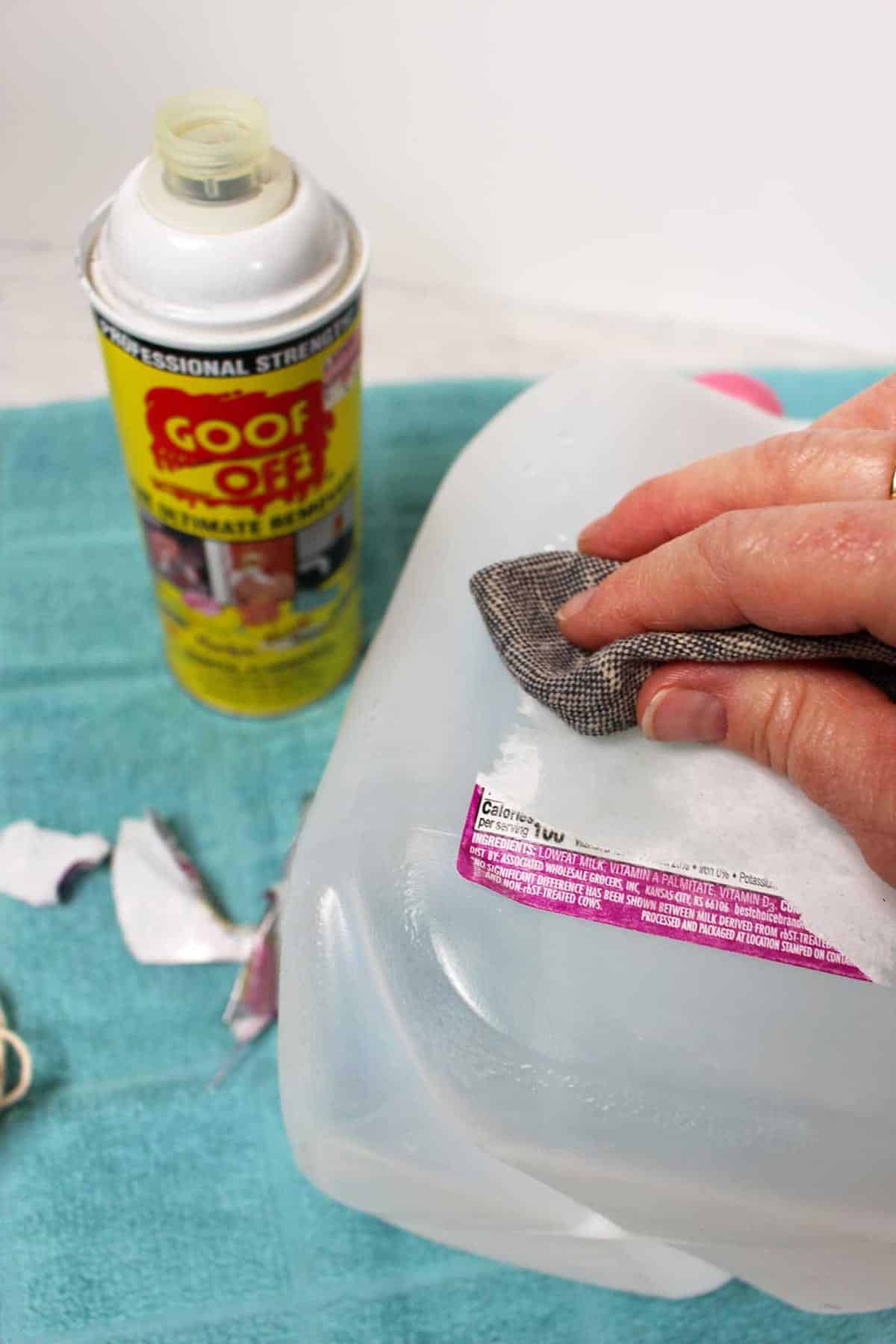 A rag rubbing the label off of a recycled milk jug, with a can of Goo Off nearby.