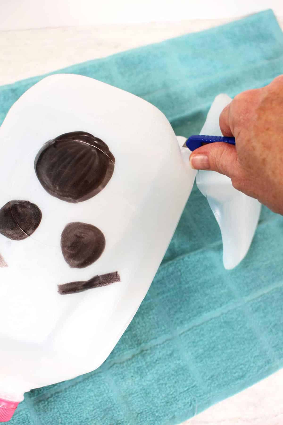 Cutting away the base of a milk jug with a ghost face drawn on the outside with a craft utility knife.